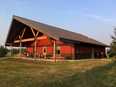 Red barn looking building with wood picnic tables on the cement patio